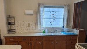 A kitchen with a white countertop, wooden cabinets, a window with curtains, and a built-in oven. - 2-bedroom in quiet neighborhood -- monthly rental perfect for traveling workers! (St. Joseph)