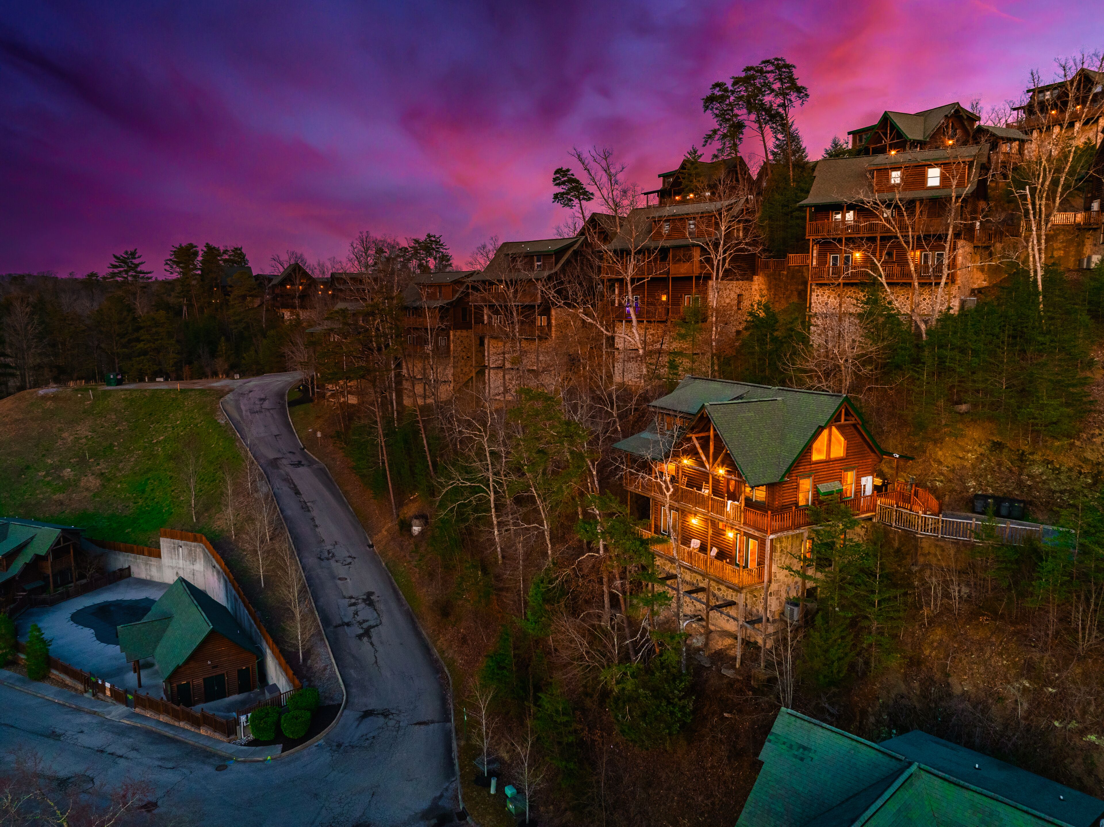 A lodge with multiple wooden buildings, a winding road, and a view of the surrounding forest.
