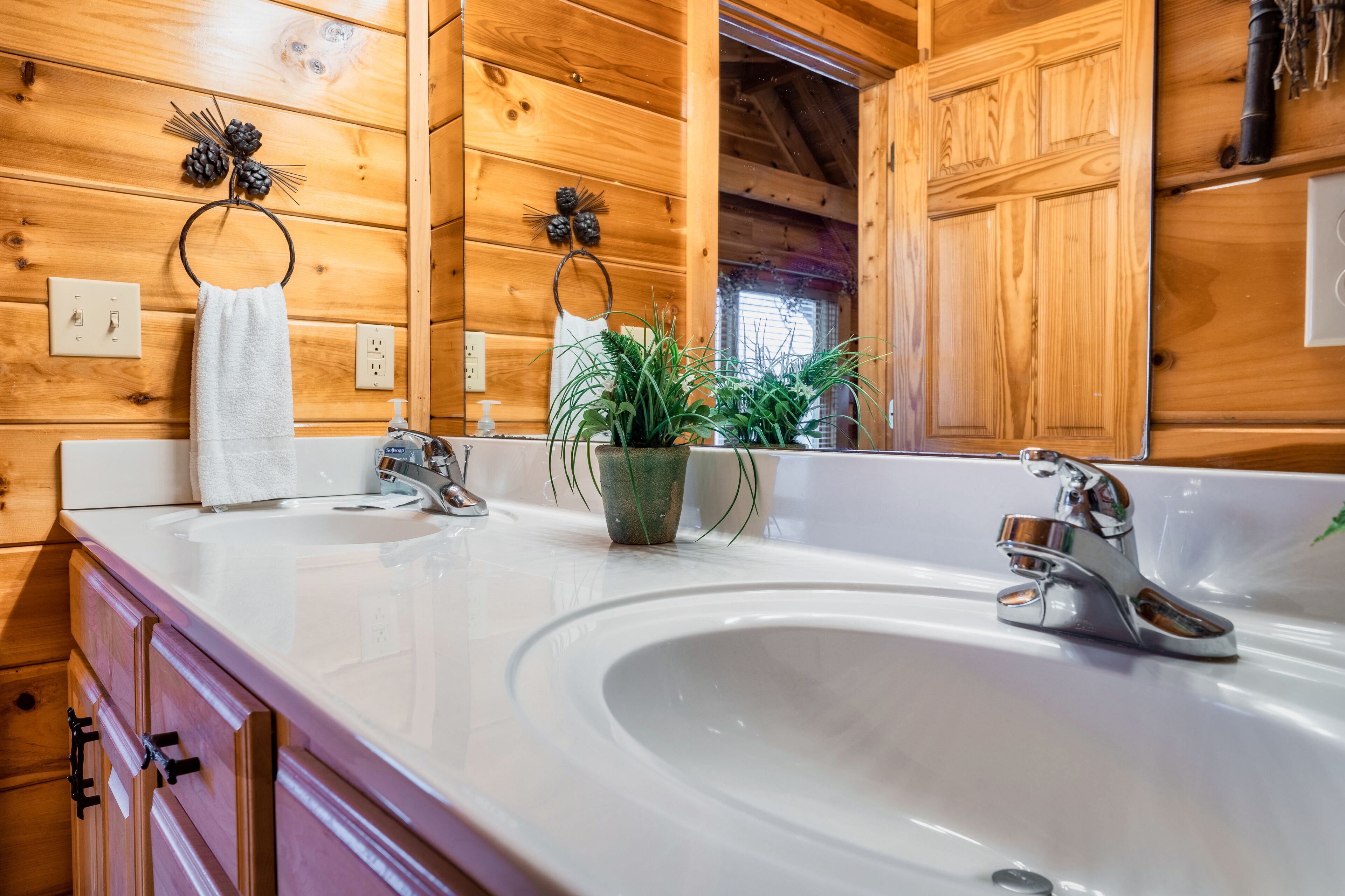 Une salle de bain rustique, avec des murs en bois, comprenant un grand lavabo, deux porte-serviettes, une plante en pot et un miroir.