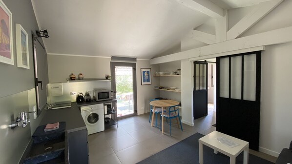 A compact kitchen with a washing machine, a microwave, and a sink. There is a dining area with a table and chairs.
