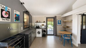 Una cocina compacta con lavadora, microondas y lavamanos. Hay una zona de comedor con una mesa y sillas.