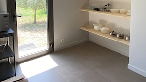 A room with a sliding glass door leading to a garden, built-in shelves with kitchenware, and a tiled floor. - Charming Guesthouse with view to countryside and Mont Ventoux (Entrechaux)