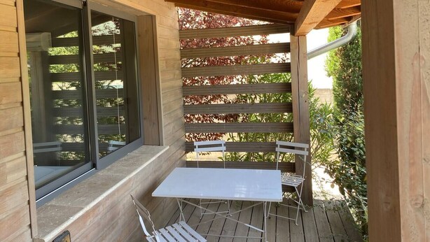 A wooden deck with a table and chairs, a pergola with red foliage, and a large window. - Charming Guesthouse with view to countryside and Mont Ventoux (Entrechaux)