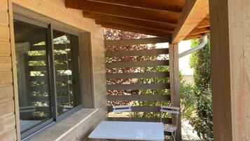 Une terrasse en bois avec une table et des chaises, une pergola ornée de feuillage rouge et une grande fenêtre.