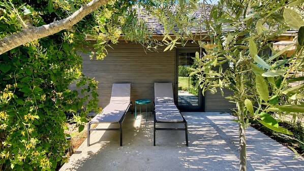 Un patio con dos sillones de descanso y una pequeña mesa, rodeado de follaje y una estructura de madera.