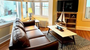 A living room with a brown leather sofa, a small table, a sailboat model, a TV, and a bookshelf. - Queen Anne's Revenge (Bar Harbor)