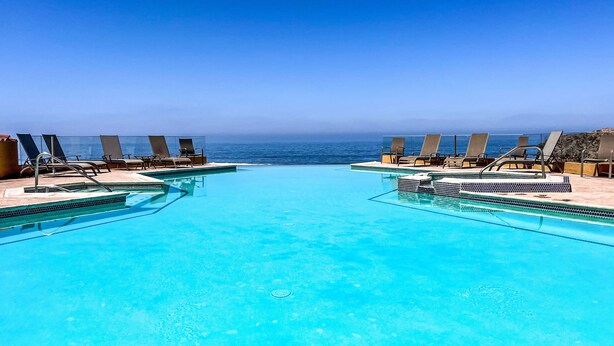 A clear blue infinity pool with lounge chairs facing the ocean, surrounded by a stone deck. - Luxury Condo/La Jolla Real/Pools & Jacuzzis/ Beach Access/ Rosarito/ Free Wifi (Rosarito)
