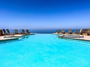 Ein klarer, blauer Infinity-Pool mit Liegestühlen, die zum Meer ausgerichtet sind, umgeben von einer Steindeckterrasse.