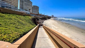 A coastal walkway with a green hedge, a sandy beach, and high-rise buildings in the background. - Luxury Condo/La Jolla Real/Pools & Jacuzzis/ Beach Access/ Rosarito/ Free Wifi (Rosarito)