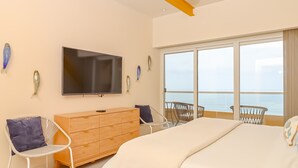 A modern bedroom with a large bed, a TV, a wooden dresser, and a balcony with a view of the sea. - Luxury Condo/La Jolla Real/Pools & Jacuzzis/ Beach Access/ Rosarito/ Free Wifi (Rosarito)