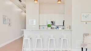 Una cocina moderna con armarios blancos, un microondas y una barra con taburetes blancos.