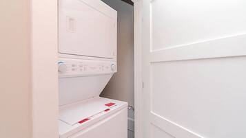 A compact laundry room with a stacked washer and dryer, a metal rack, and a white door.