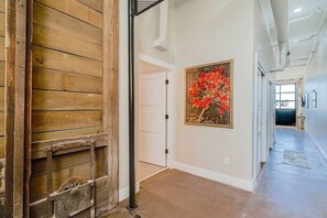Un couloir avec une porte en bois, une porte blanche et un tableau représentant des fleurs rouges accroché au mur.