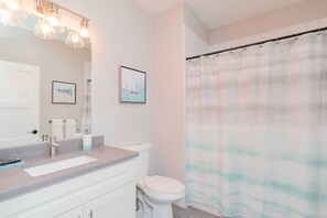Une salle de bain avec un lavabo blanc, des toilettes et un rideau de douche. Deux tableaux encadrés sont accrochés au mur.
