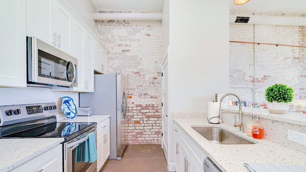 Una cocina moderna con armarios blancos, una pared de ladrillo decorativa, electrodomésticos de acero inoxidable y una encimera de granito.