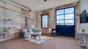 Un salón amplio con paredes de ladrillo visto, un ventanal grande y un ventilador de techo.