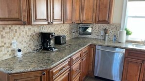 Una cocina con gabinetes de madera, encimeras de granito, cafetera, microondas y lavavajillas.