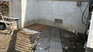 Fachada de una casa con un patio empedrado, una pequeña terraza de madera y una ventana.