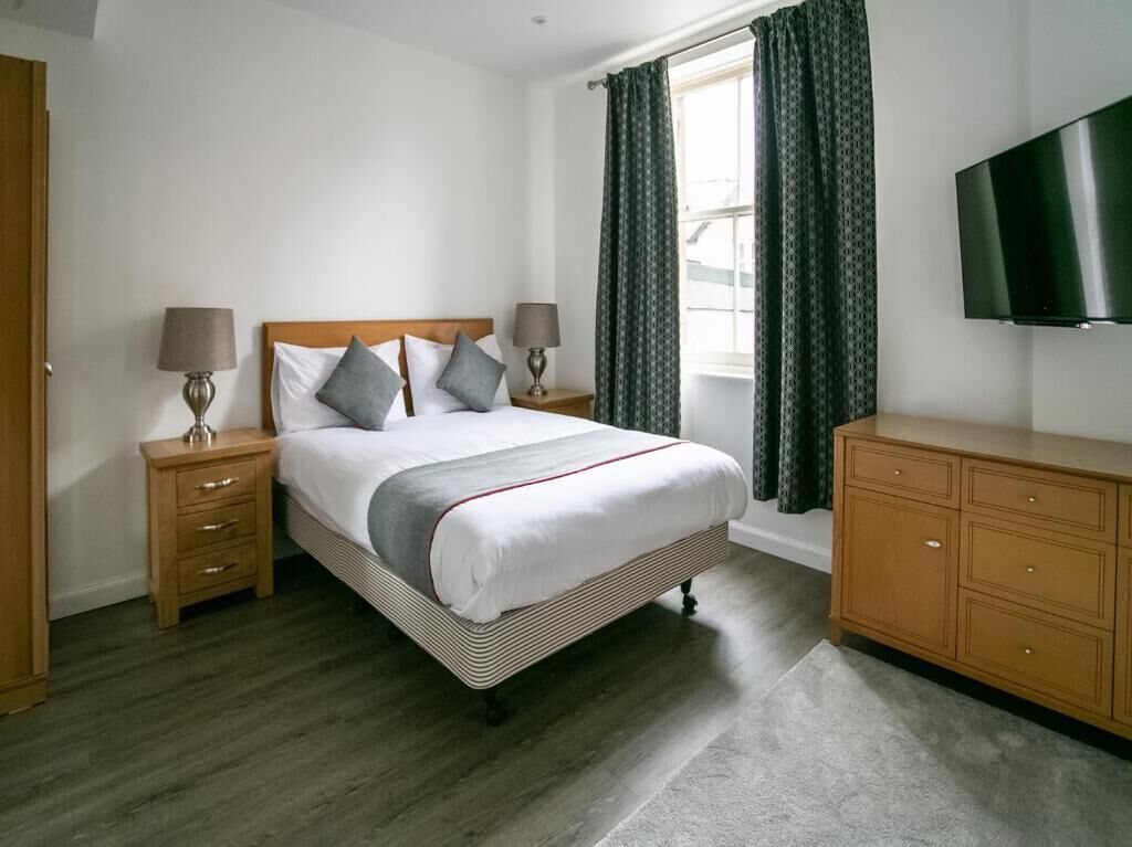 A neatly arranged bedroom with a bed, bedside tables, a dresser, and a TV mounted on the wall.