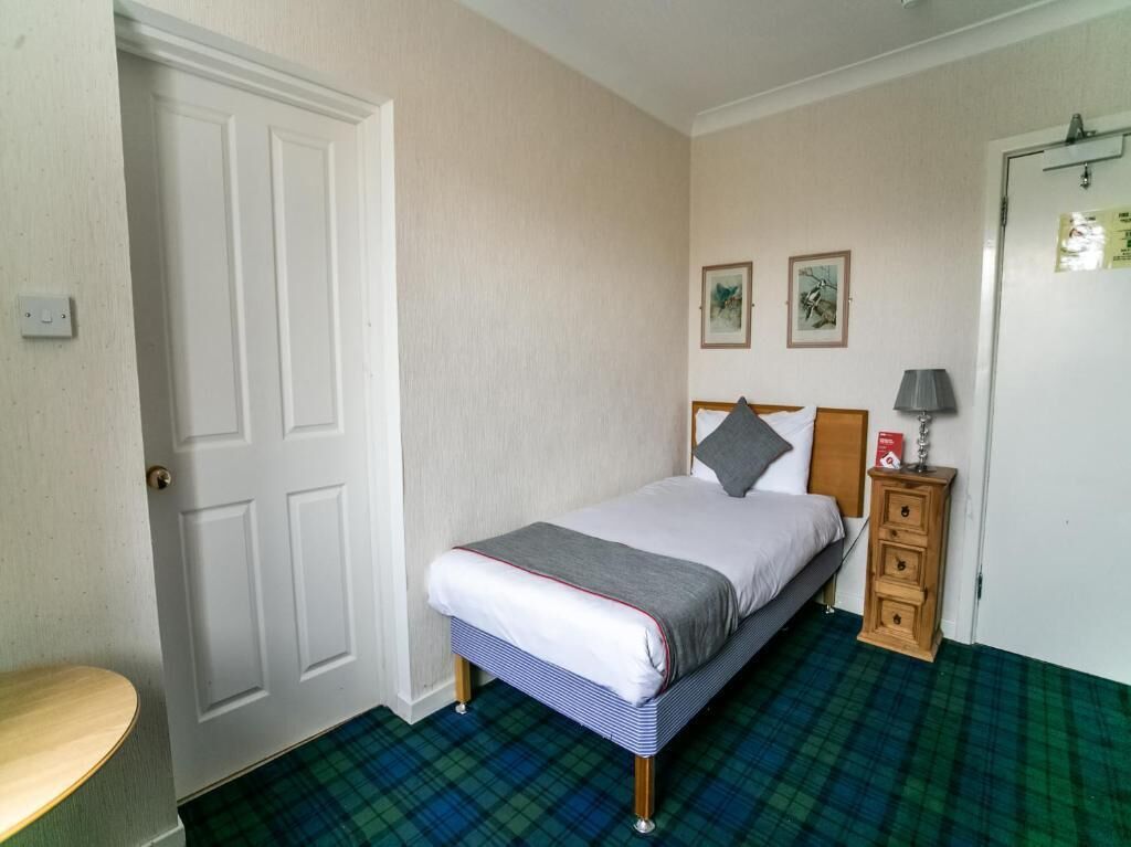 A bedroom with a bed, a nightstand, a lamp, and a door.