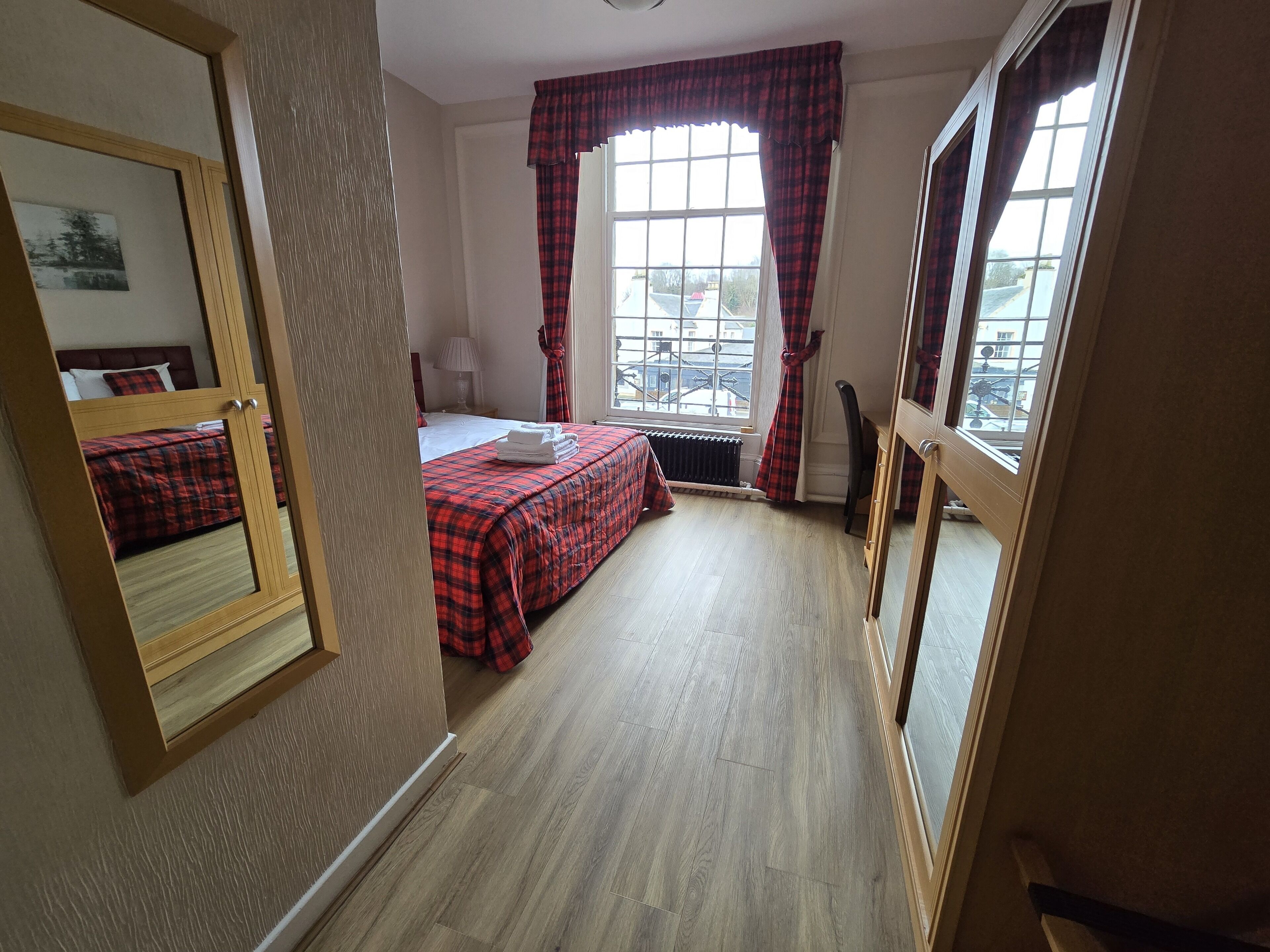 A hotel room with a bed, a radiator, a window with curtains, and a mirror.