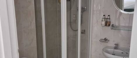 A bathroom with a glass-enclosed shower, a toilet, and a sink with a mirror above it.