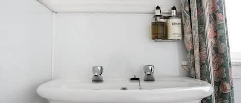 A bathroom with a white pedestal sink, a round mirror, and two bottles of toiletries on a shelf.