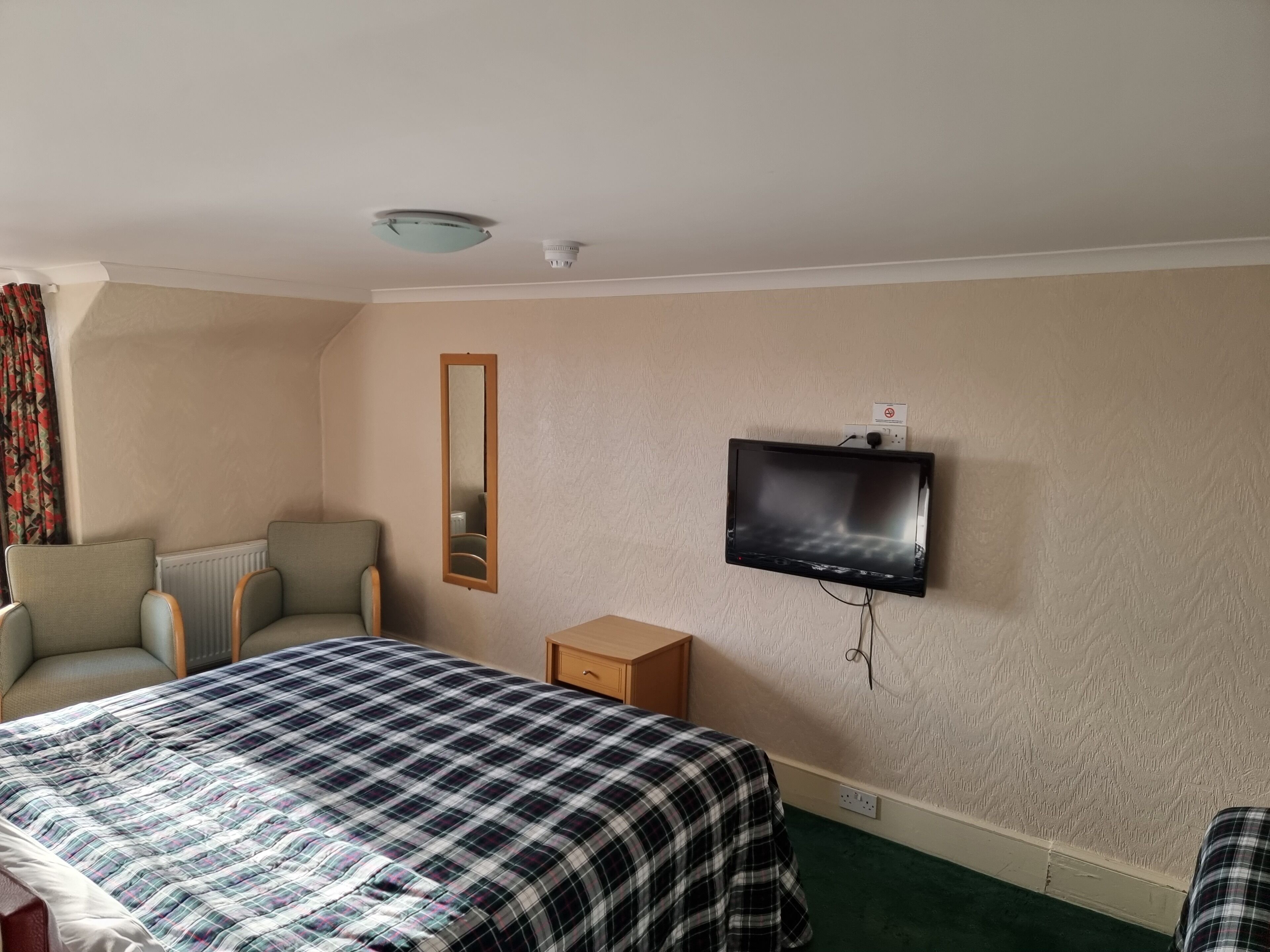 A hotel room with a bed, a chair, a television mounted on the wall, and a small wooden nightstand.