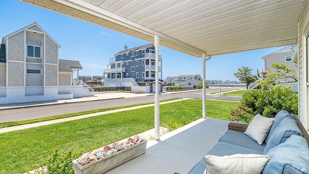A covered outdoor seating area with a view of residential buildings and a road. - Bay-View Bungalow, Dogs Welcome, Parking — Sleeps 9, Single Level (Ventnor City)