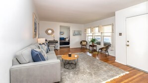 A modern living room with a sofa, coffee table, and a view through a window. - Bay-View Bungalow, Dogs Welcome, Parking — Sleeps 9, Single Level (Ventnor City)