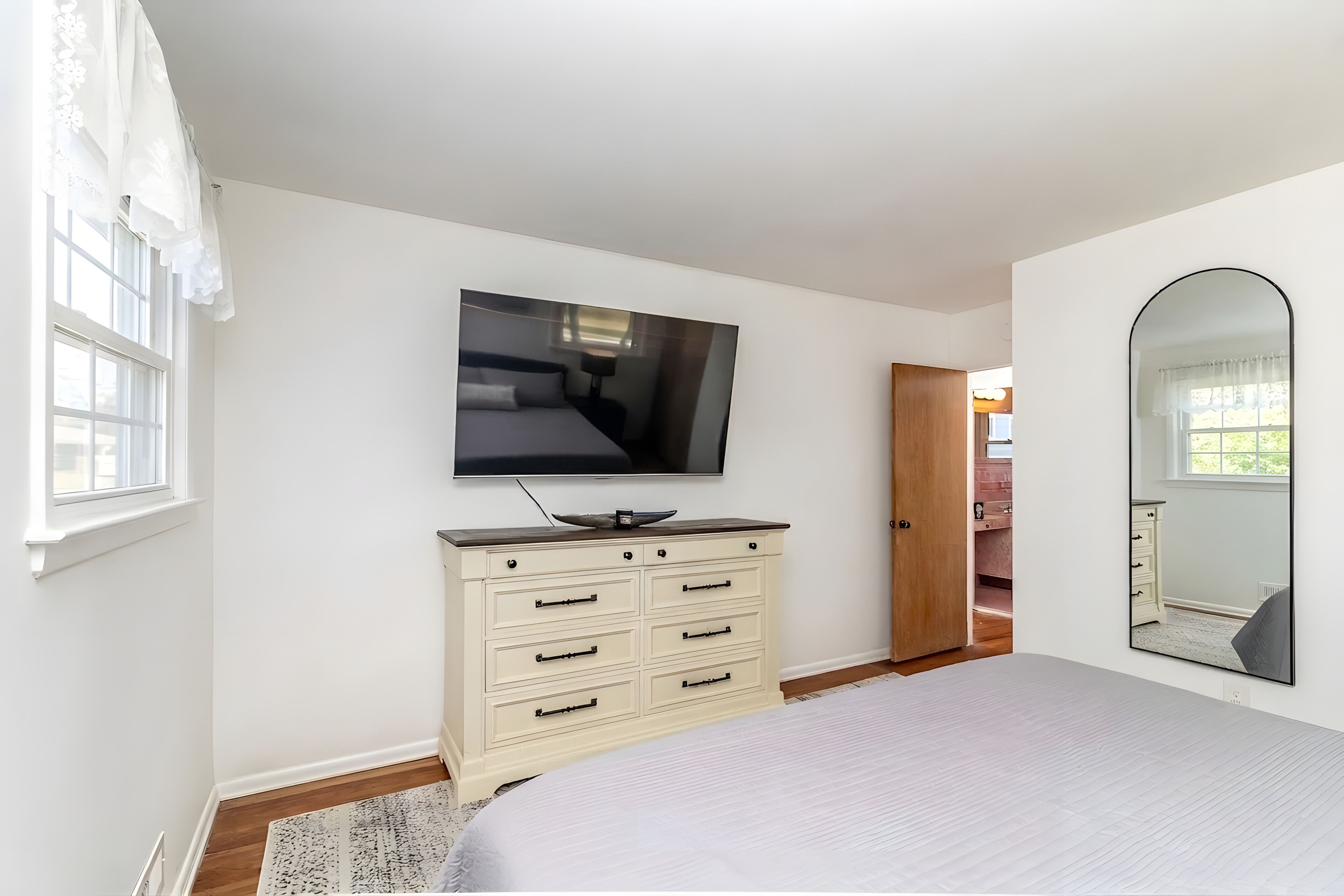 A bedroom with a bed, a dresser, a television, a mirror, and a window.
