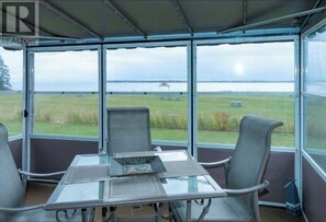 A conservatory with a glass table and two chairs, overlooking a grassy field and a body of water. - Experience tranquility by the sea, Magnificent views, Romantic charm. (Lower Montague)