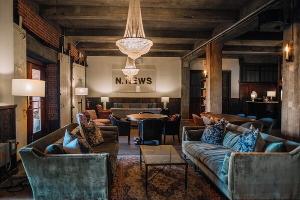 A spacious lounge area with a chandelier, comfortable seating, and a prominent 'N. NEWS' sign on the wall.