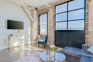 Un salon moderne avec des murs en briques apparentes, une grande fenêtre, un téléviseur à écran plat, un canapé, une table basse et un bureau.