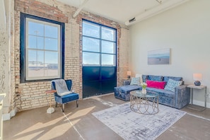 A spacious room with a large window, a blue sofa, a chair, and a coffee table.