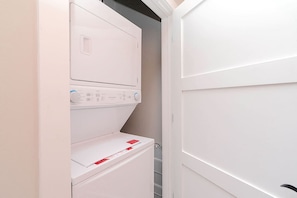 A compact laundry room with a stacked washer and dryer, a metal rack, and a white door.