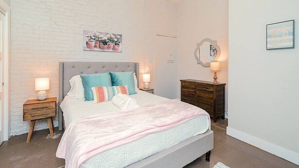 Ein Schlafzimmer mit einem Bett, zwei Nachttischen, einer Kommode und einem wandmontierten Spiegel.