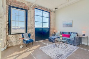A spacious room with a large window, a blue sofa, a chair, and a small table.