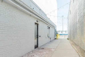 A narrow alleyway with a white brick building, a metal door, and a concrete pathway.