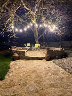 An outdoor patio area with a stone table and chairs, surrounded by terracotta pots and a string of lights. - Cantinho Daldeia - Rural House with Pool (Guarda)