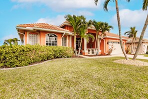 A house with a red-tiled roof, a front porch, and palm trees.