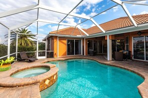 A swimming pool with a hot tub, surrounded by a covered patio with seating and a view of a palm tree.