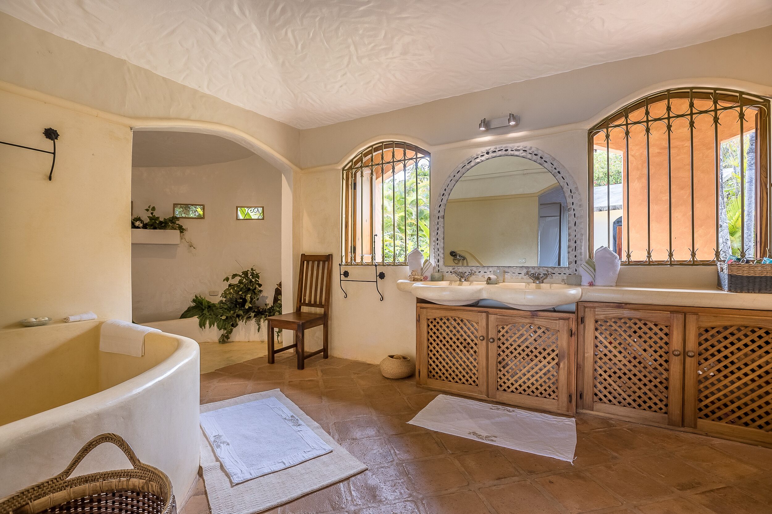 Un baño con una bañera independiente, armarios de madera, un espejo grande y una ventana con barrotes.