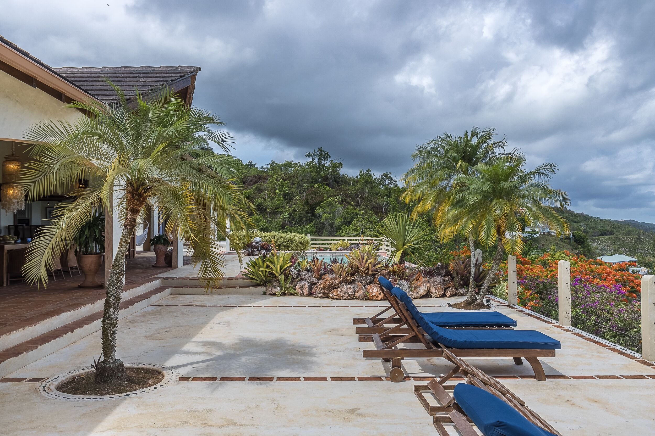 A pool area with lounge chairs, palm trees, and a view of a mountainous landscape.