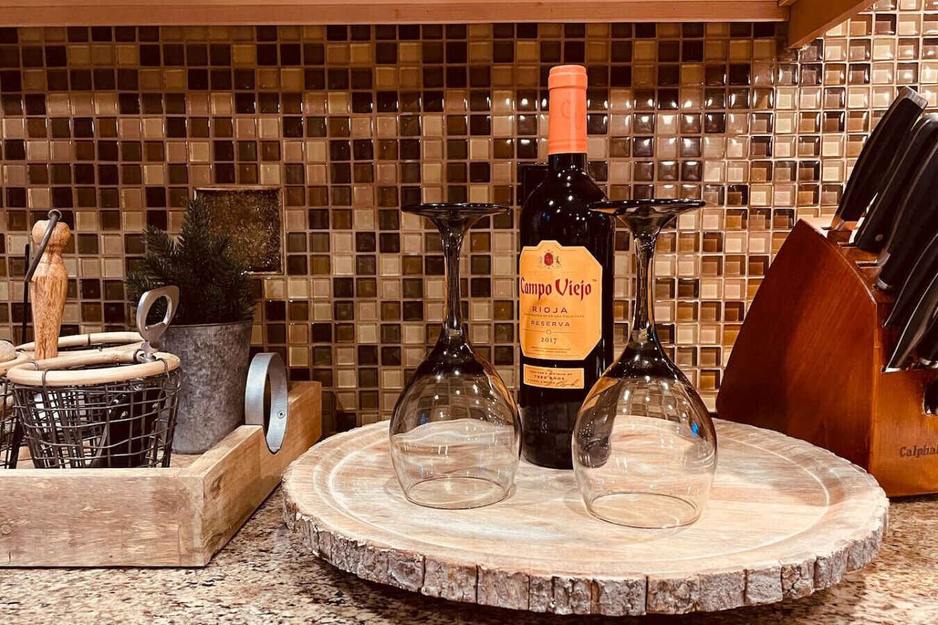 Een aanrecht met een fles Campo Viejo Rioja Reserva 2017, twee wijnglazen, een houten snijplank en een messenblok.