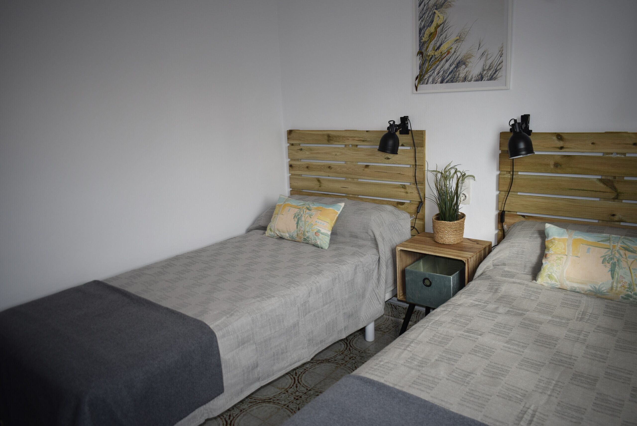 A bedroom with two single beds, wooden headboards, bedside tables with lamps, and a wall-mounted plant.