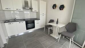 A modern kitchen with white cabinets, a built-in oven, and a dining area with a table and chairs. - Apartments Roko - One bedroom apartment with balcony and sea view (A2) (Sveti Filip i Jakov)