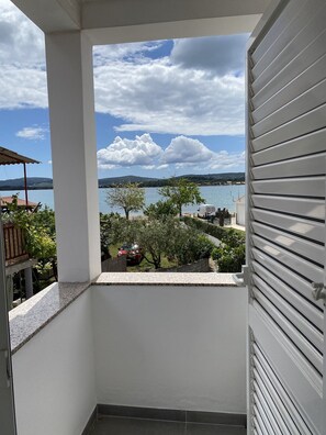 A balcony with a view of a lake and distant hills, a red car parked nearby, and a white door with horizontal slats. - Apartments Roko - One bedroom apartment with balcony and sea view (A2) (Sveti Filip i Jakov)
