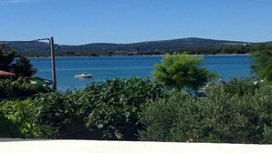A coastal view with a boat on the water, greenery in the foreground, and hills in the background. - Apartments Roko - One bedroom apartment with balcony and sea view (A2) (Sveti Filip i Jakov)