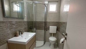 A modern bathroom with a glass shower enclosure, a white sink, and a toilet.